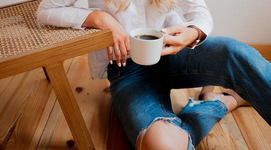 person sitting on wooden floor against chair holding cup of coffee